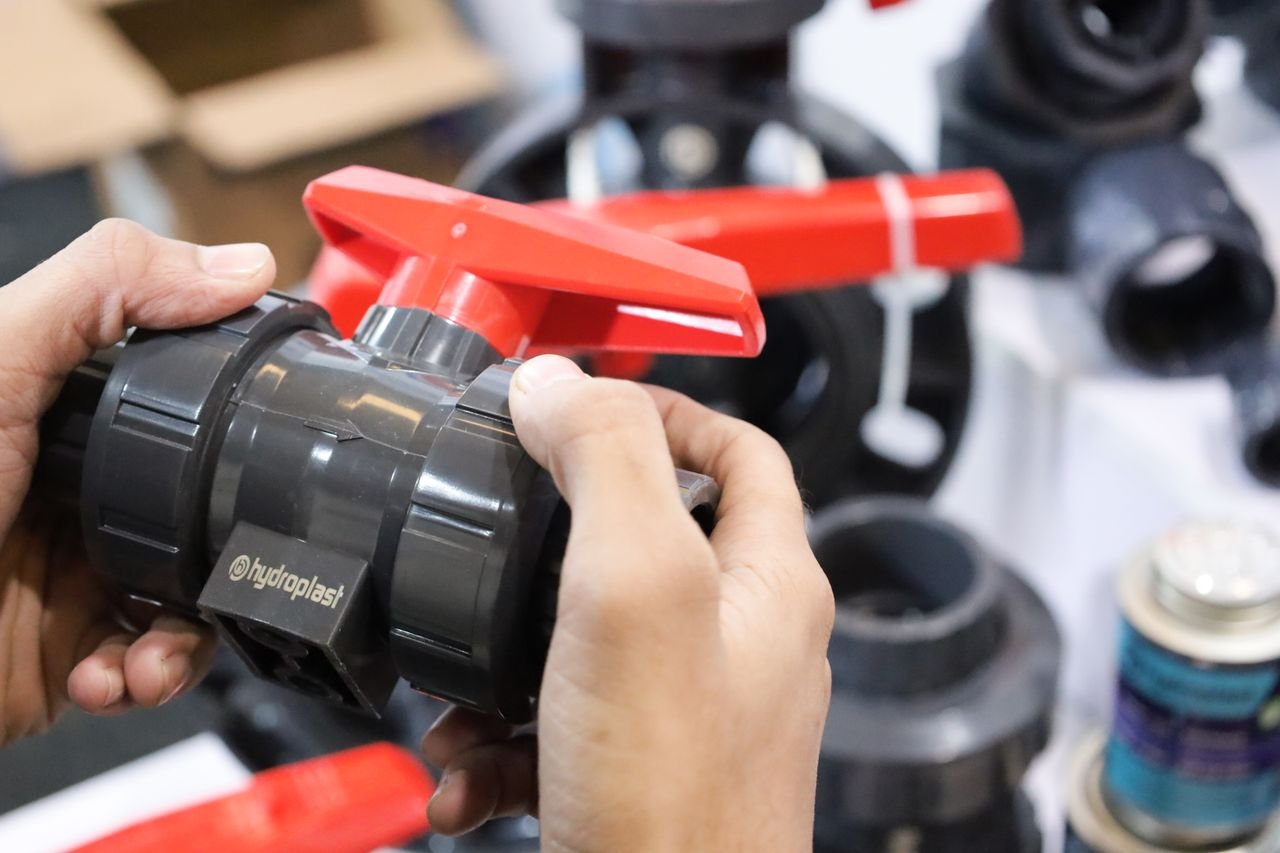 Services Close-up of hands examining a Hydroplast industrial valve at a trade expo.