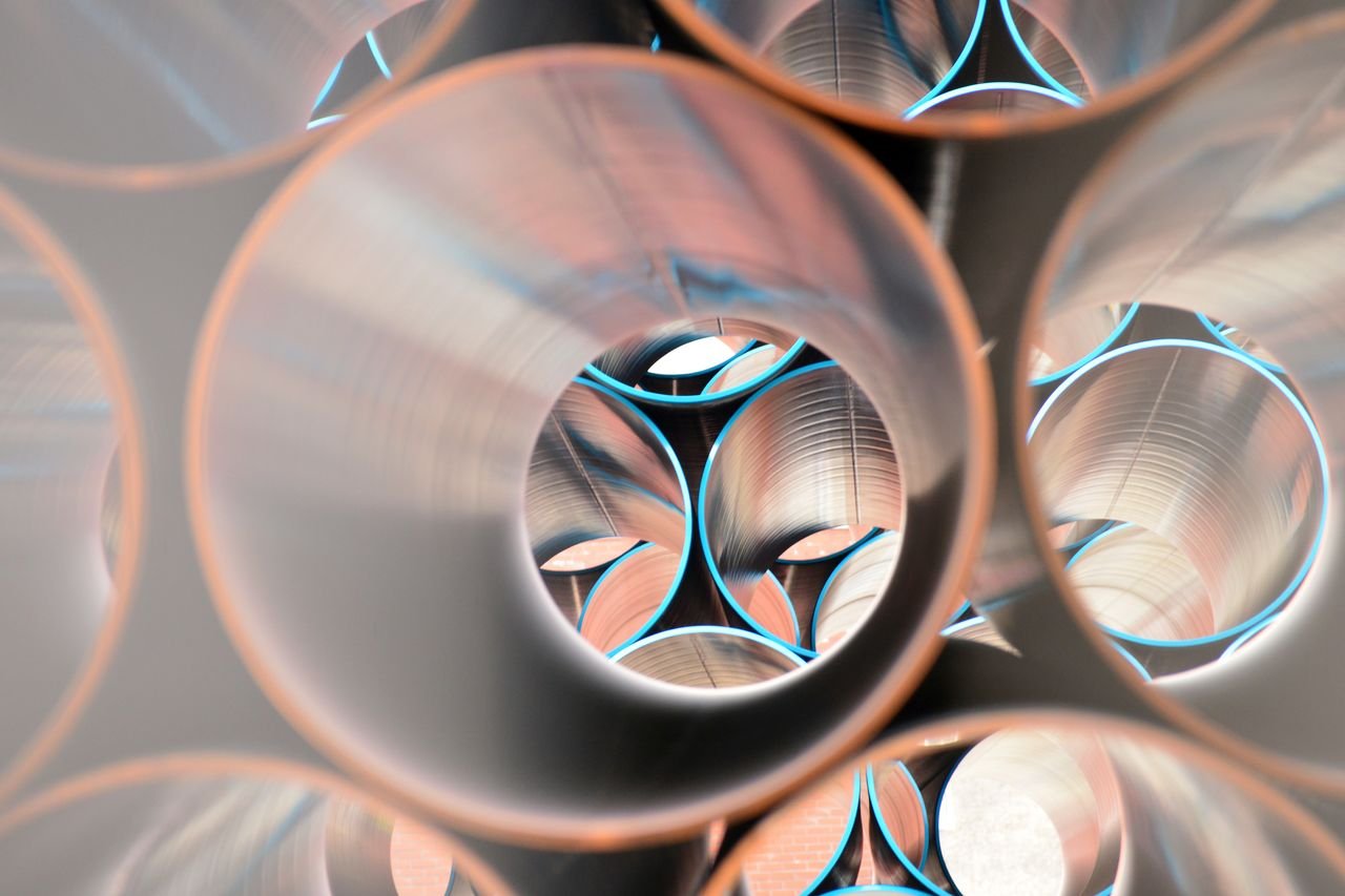Services Artistic perspective of stacked steel tubes creating a geometric pattern with reflections.