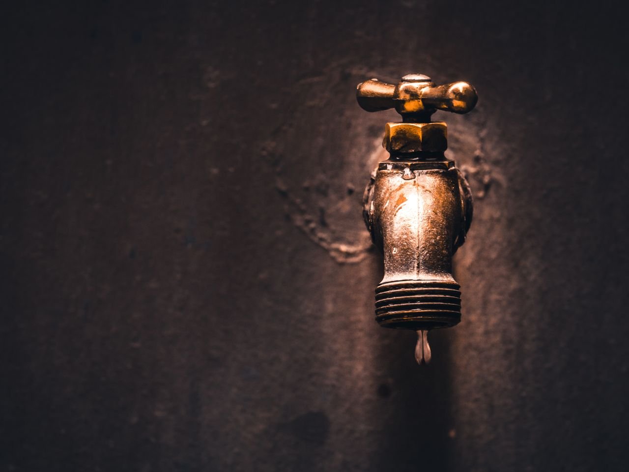 Services A close-up view of a vintage brass faucet with a single water droplet against a dark background.