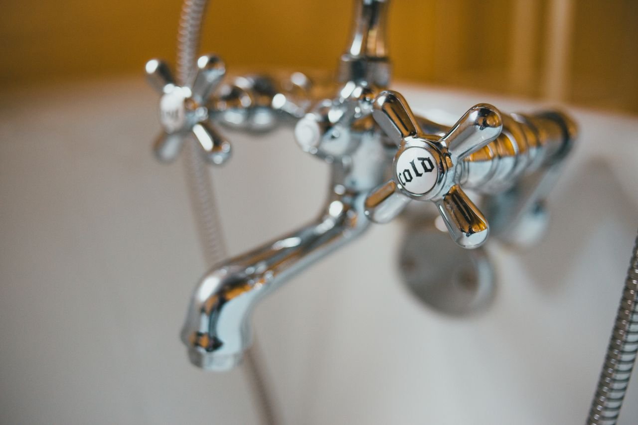 Services Detailed close-up of a vintage chrome bathtub faucet with a cold water knob in focus.